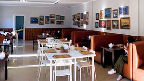 A dining area with white tables and chairs, a sofa, and framed artwork on the walls. - ololoFamily (Cholpon-Ata)