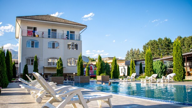 A pool area with lounge chairs and a building with multiple windows and balconies. - ololoFamily (Cholpon-Ata)