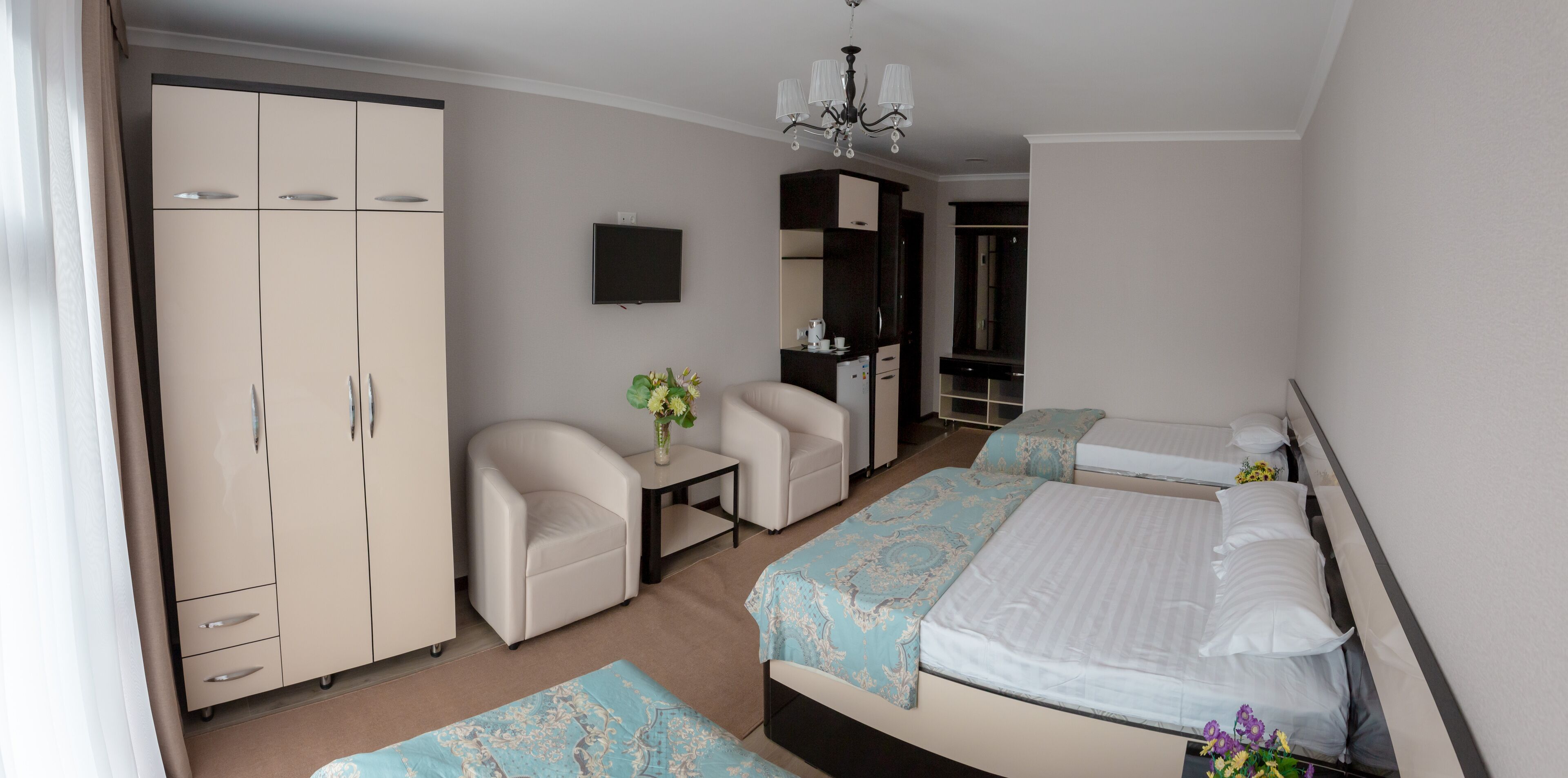 A hotel room with a bed, two bedside tables, a chair, a wardrobe, and a TV.