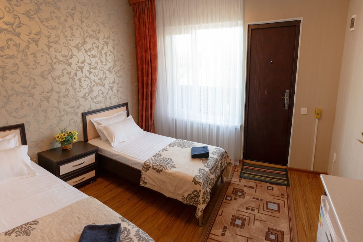 A hotel room with two beds, a nightstand with a vase of flowers, a wooden floor, and a patterned rug.
