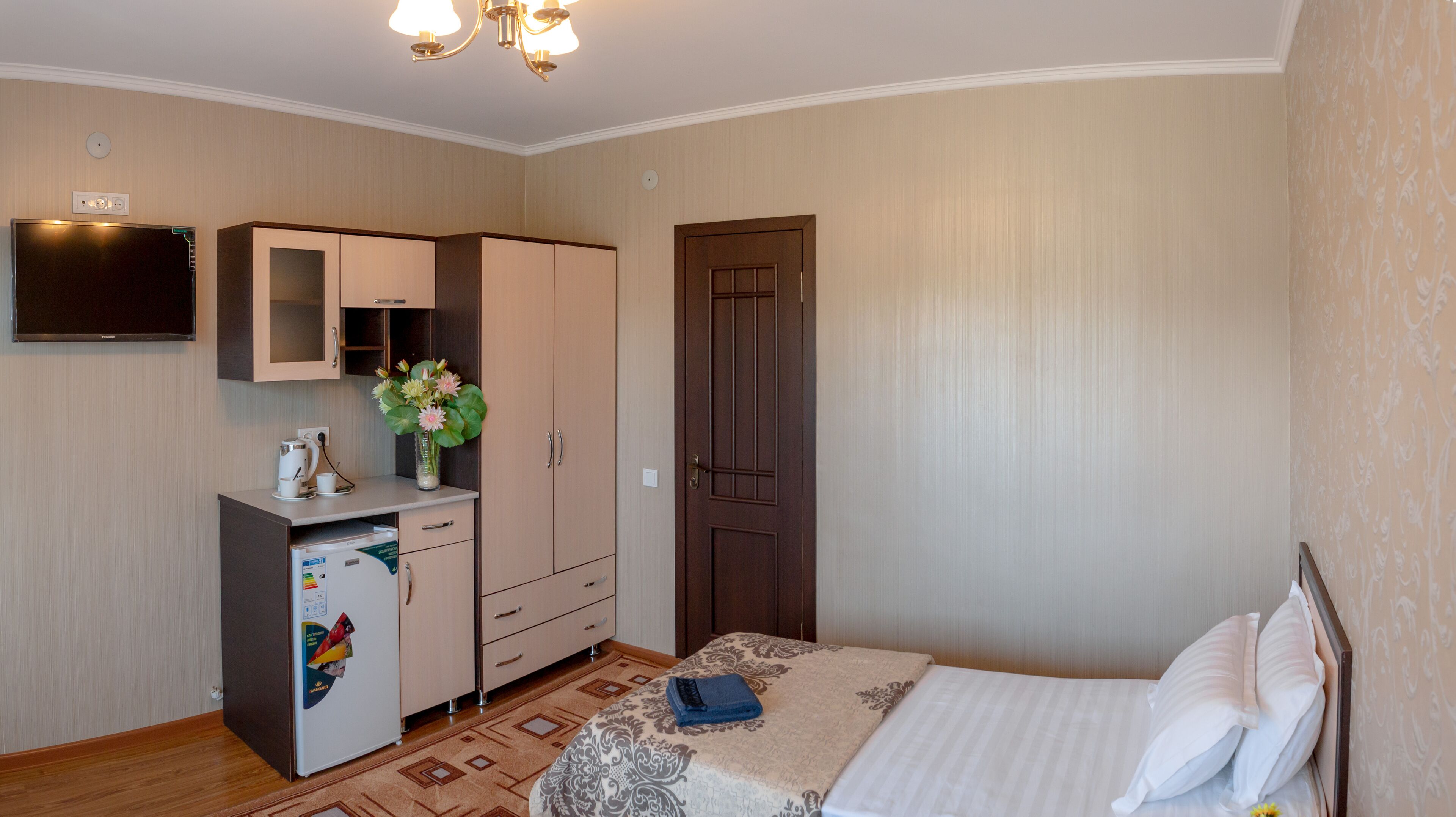 Une chambre à coucher avec un lit, un bureau avec un ordinateur, une armoire, une télévision et une porte.