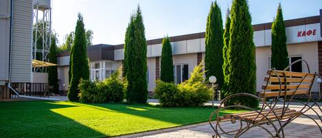 A courtyard with a paved walkway, a bench, and neatly trimmed hedges.