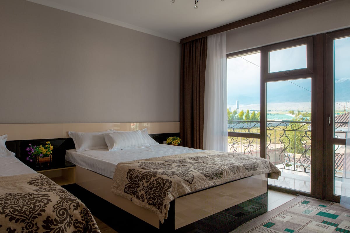 A hotel room with two beds, a large window with a view, and a balcony.