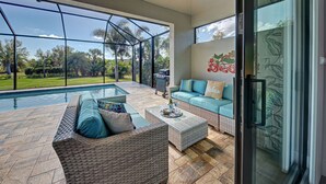 A spacious patio with a pool, wicker furniture, and a sliding glass door leading to a lush garden. - Baby SeaTurtle | Pool | Sunshelf | Tiki Bar | Office (Rotonda West)