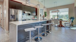 A modern kitchen with a stainless steel refrigerator, a built-in oven, and a large island with bar stools. - Baby SeaTurtle | Pool | Sunshelf | Tiki Bar | Office (Rotonda West)