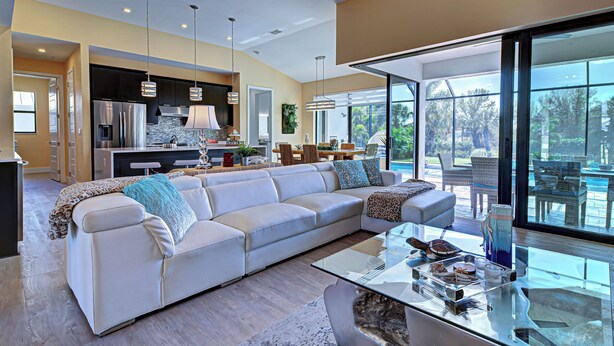 A modern living room with a large sectional sofa, a glass coffee table, and a view of the outdoors. - Baby SeaTurtle | Pool | Sunshelf | Tiki Bar | Office (Rotonda West)