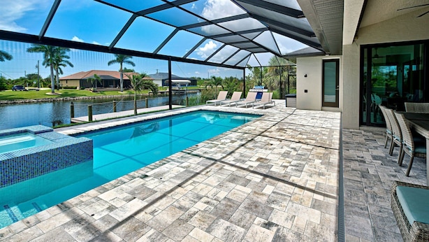 A swimming pool with a glass enclosure, a patio with outdoor furniture, and a view of a residential area. - Azure Paradise | Canal View | Dock | 2 Masters | Spa (Port Charlotte)