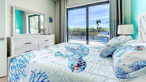A bedroom with a large bed, a dresser, a mirror, and a view of the outdoors. - Azure Paradise | Canal View | Dock | 2 Masters | Spa (Port Charlotte)