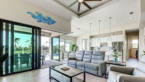 A spacious living room with a large gray sofa, a coffee table, and a dining area with a glass-top table. - Azure Paradise | Canal View | Dock | 2 Masters | Spa (Port Charlotte)