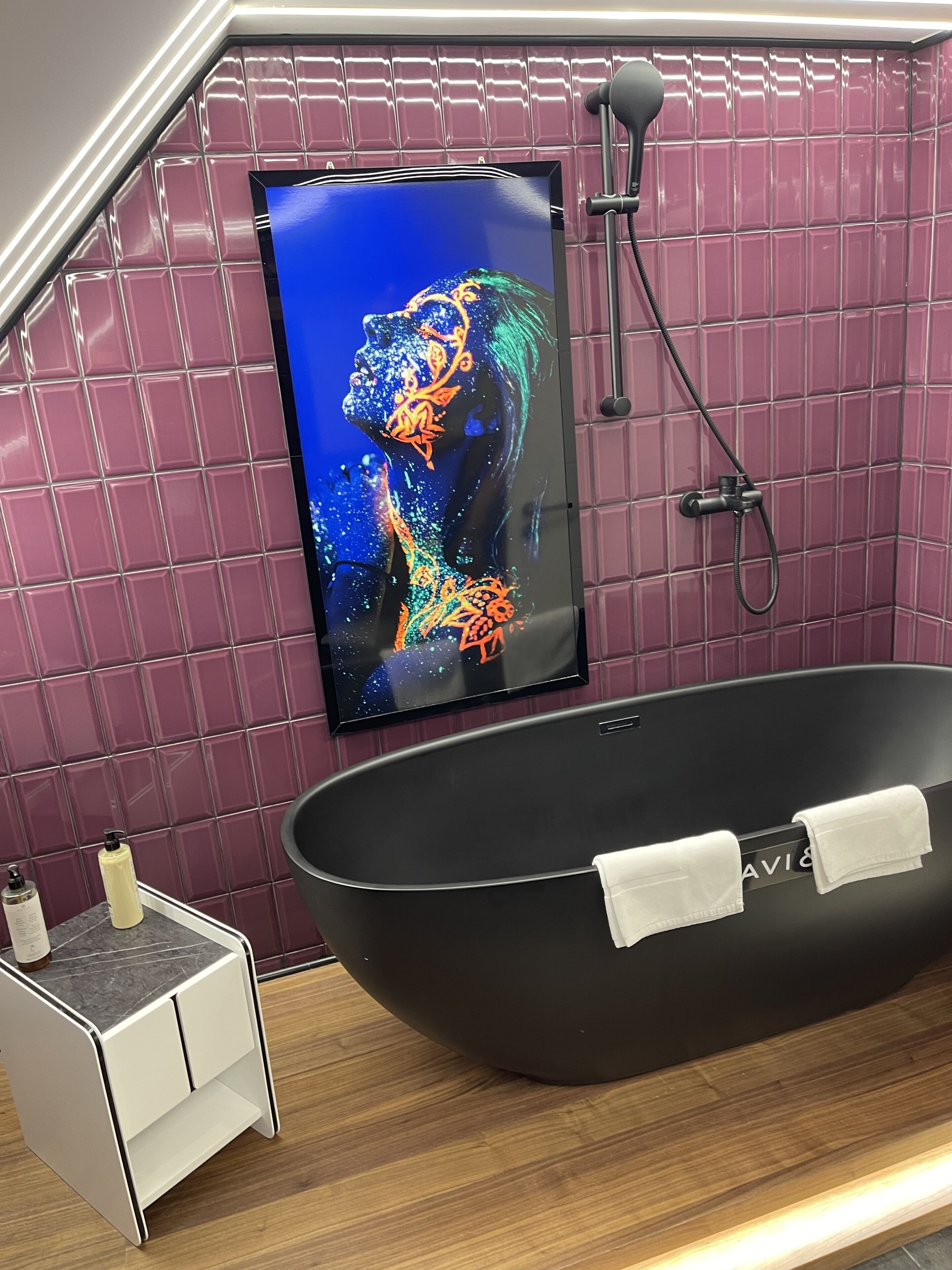 Un baño moderno con una bañera independiente, un cabezal de ducha y un televisor grande montado en la pared que muestra una imagen colorida.