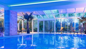 An indoor swimming pool with clear glass walls, lounge chairs, and potted plants. - Residenz Seehotel Berlin Brandenburg (Mittenwalde)