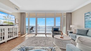 Relax in this stylish living room with a large balcony, featuring a flat-screen TV, comfortable seating, and a beautiful view.