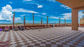 Relax on the sun-kissed beachside terrace, surrounded by palm trees and a clear sky, with comfortable loungers at your disposal.