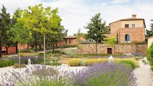 Ein traditionelles Gebäude mit einer Steinauffassade, umgeben von einem gepflegten Garten mit Lavendel und anderen Pflanzen.
