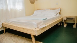 A single wooden bed with white linens in a room with a green floor and a woven wall decoration. - 
🏡 Peaceful Family Retreat in Arusha – Near National Parks & City Center (Arusha)