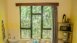 A dining area with a wooden table set for four, a window with curtains, a sink, and a shelf with kitchen items. - 
🏡 Peaceful Family Retreat in Arusha – Near National Parks & City Center (Arusha)