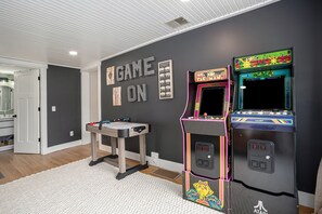 Ein Raum mit zwei Spielautomaten, einem Tisch mit einem Gesellschaftsspiel und einer Tür zu einem weiteren Raum.