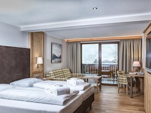 A hotel room with a large bed, a desk, a chair, a balcony with curtains, and a view of the outside. - DZ Rofan 4-6 ÜN - Hotel Pfandler (Pertisau)