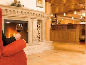 A fireplace with a glass of wine, a wooden bench, and a bar area with bottles. - DZ Rofan 4-6 ÜN - Hotel Pfandler (Pertisau)
