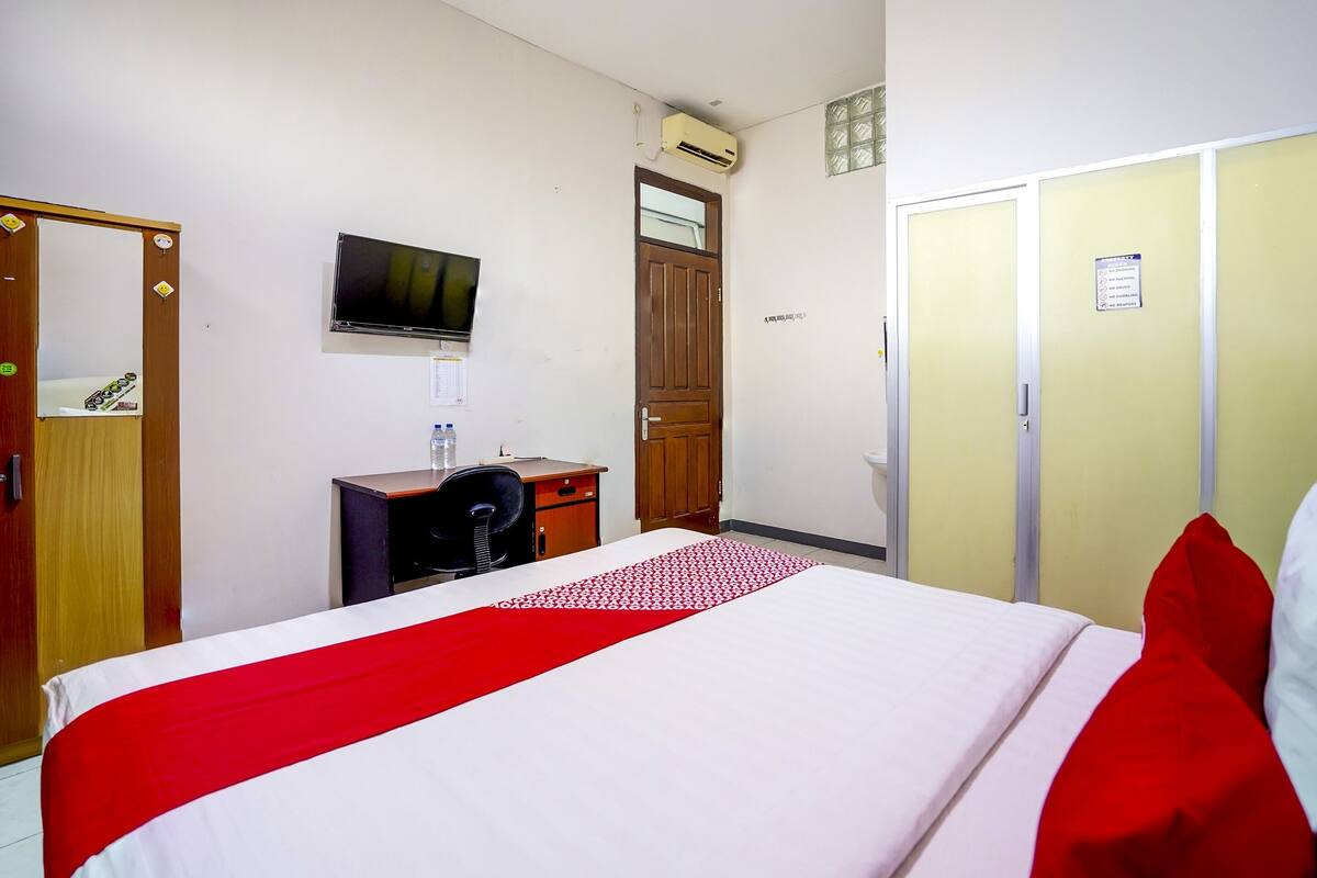 Habitación de hotel con cama, escritorio, silla, televisor y armario.