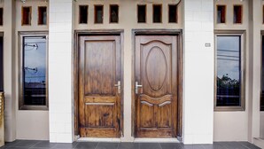 Une façade d’immeuble avec deux portes en bois, un sol carrelé et de petites fenêtres.