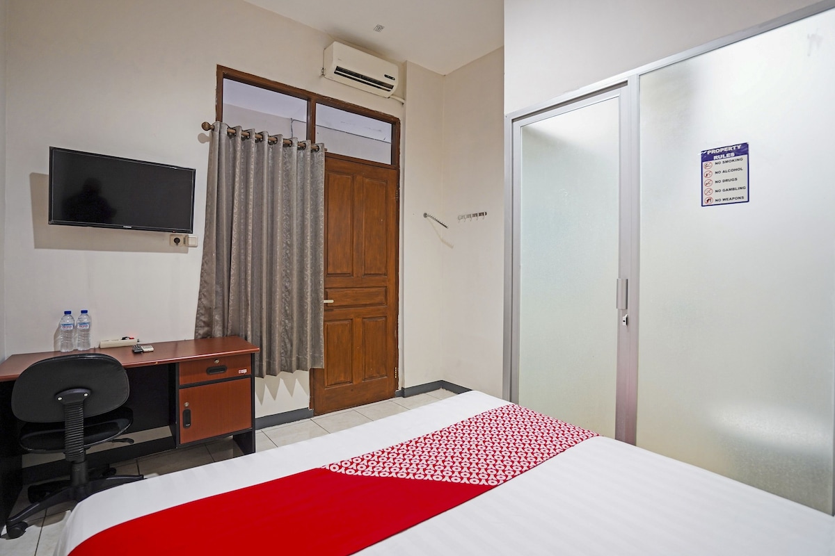 Une chambre d’hôtel équipée d’un lit, d’un bureau, d’une télévision, d’une armoire et d’un panneau indiquant le règlement de l’établissement.