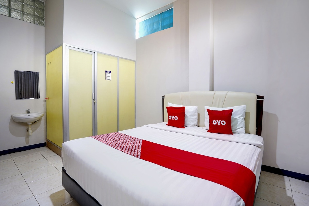 Une chambre d’hôtel avec un lit, une armoire jaune, un lavabo et une fenêtre.