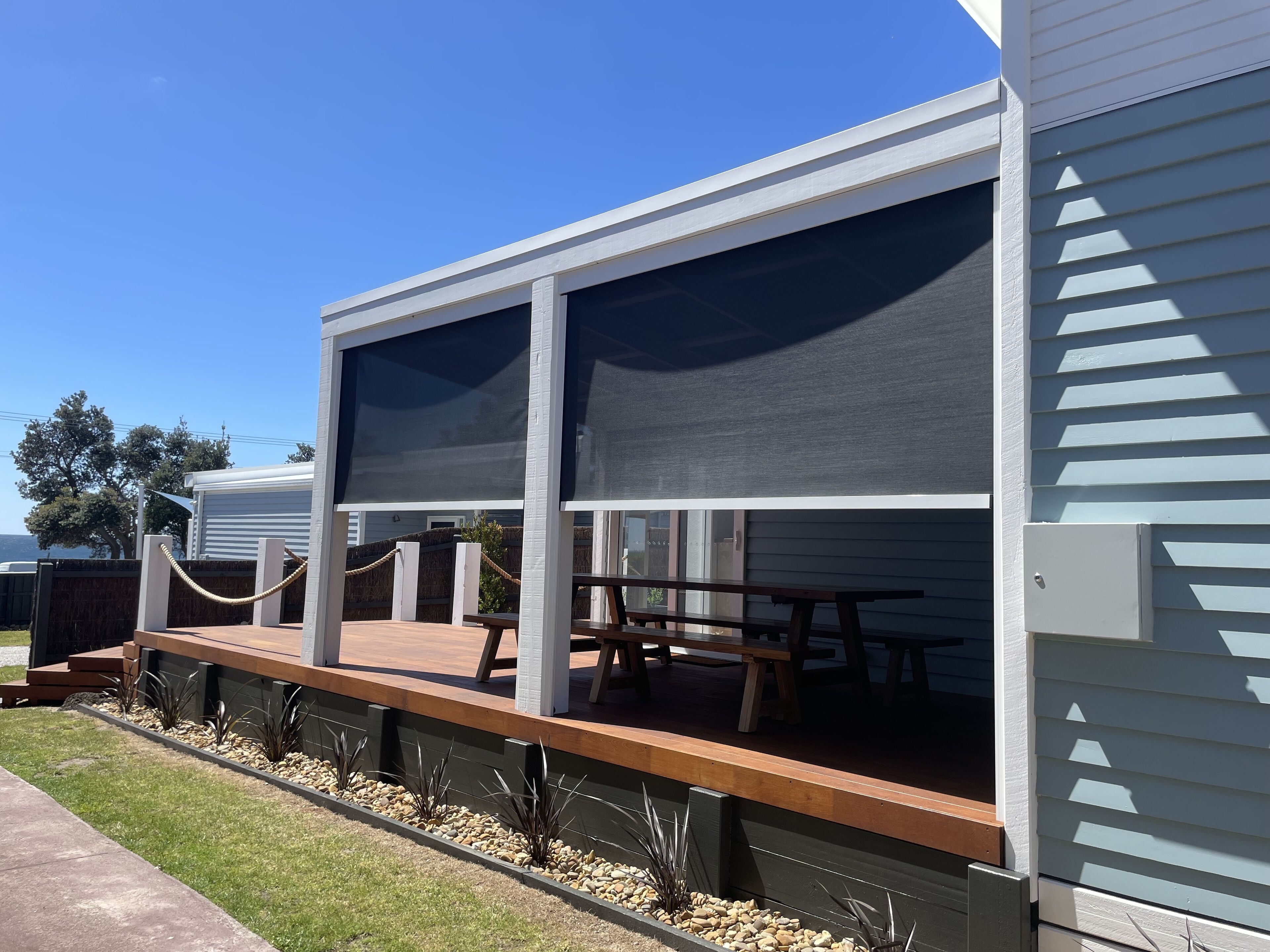 A modern outdoor patio with a wooden deck, a covered seating area, and a view of the surrounding landscape.