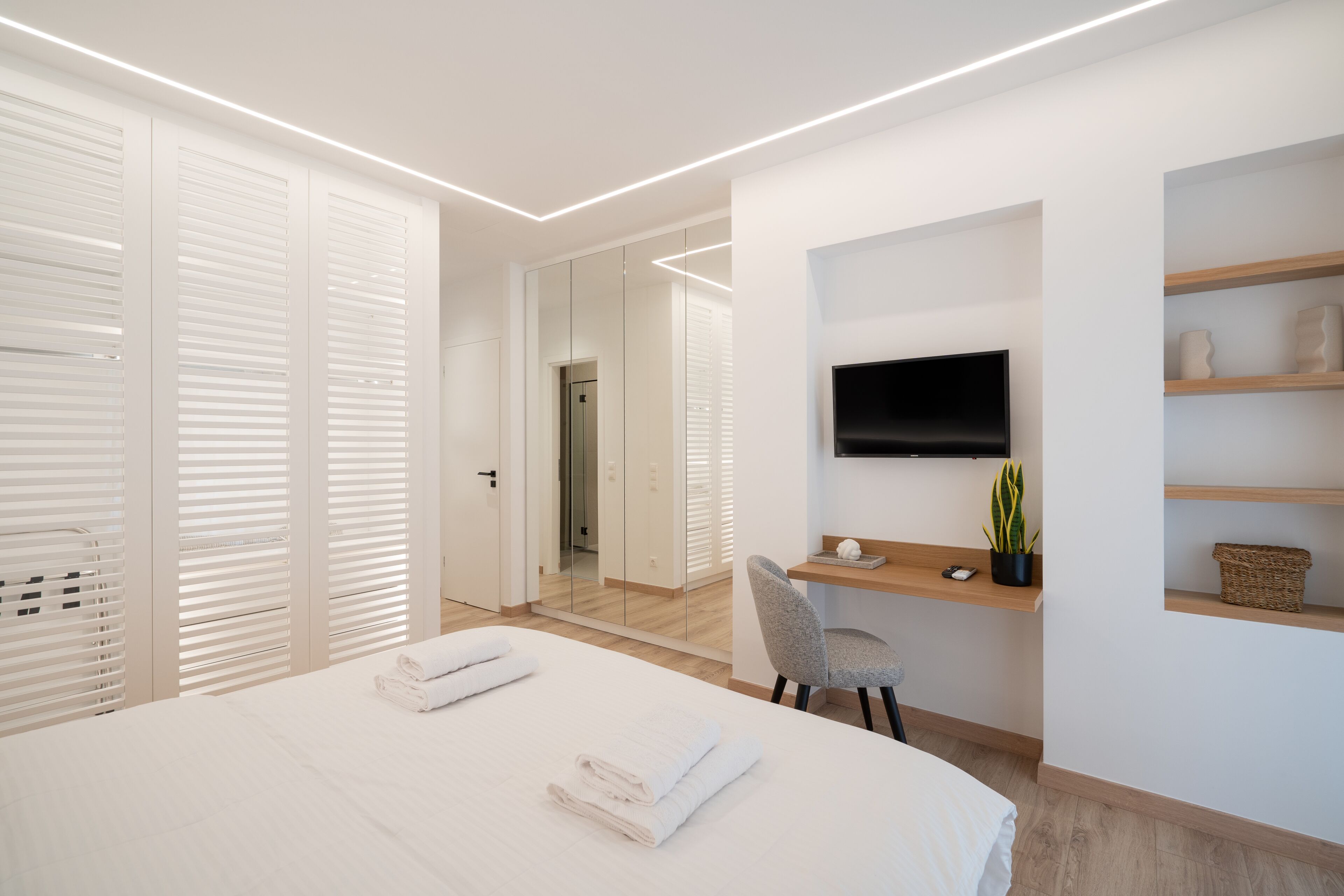 Una habitación de hotel moderna con una cama grande, un escritorio con una silla, un televisor de pantalla plana y una pequeña planta.