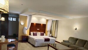 Quarto de hotel com cama, sofá, mesa de jantar e abajur.