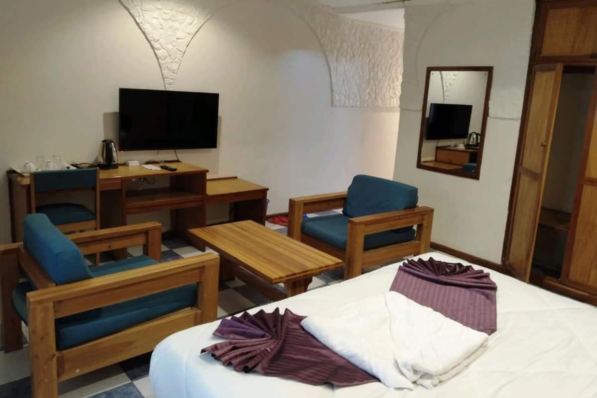 A hotel room with a bed, two wooden chairs, a small wooden table, a TV, and a mirror.