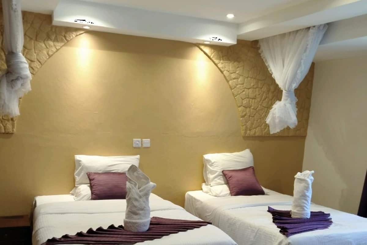 A hotel room with two beds, each with white linens and purple accents, a stone accent wall, and a ceiling with recessed lighting.