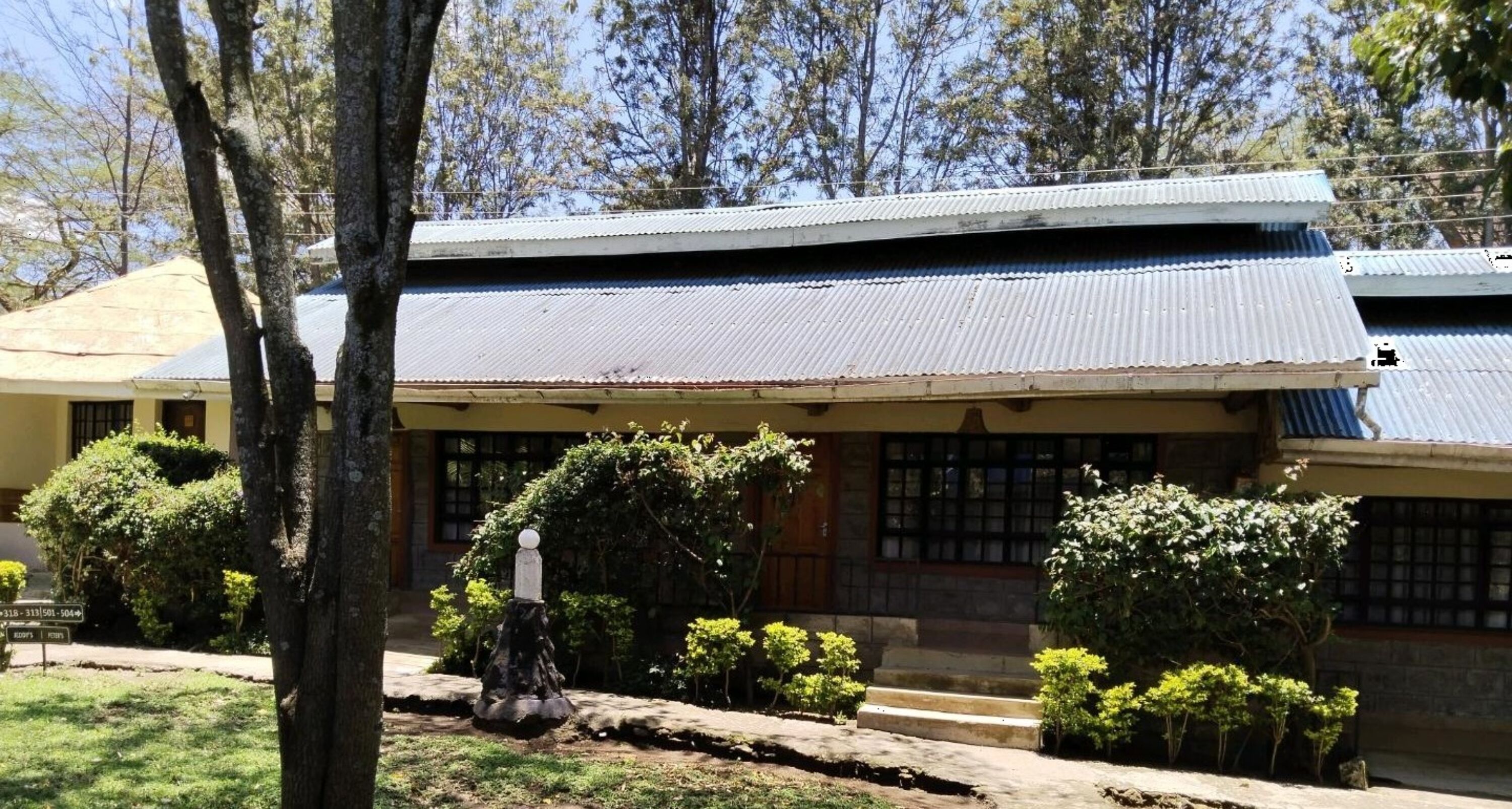 A traditional building with a tiled roof, a stone base, and a small garden with shrubs and a stone lantern.
