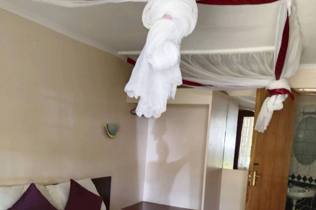 A hotel room with a bed, a nightstand, a wall-mounted shelf, and a bathroom visible through an open door.
