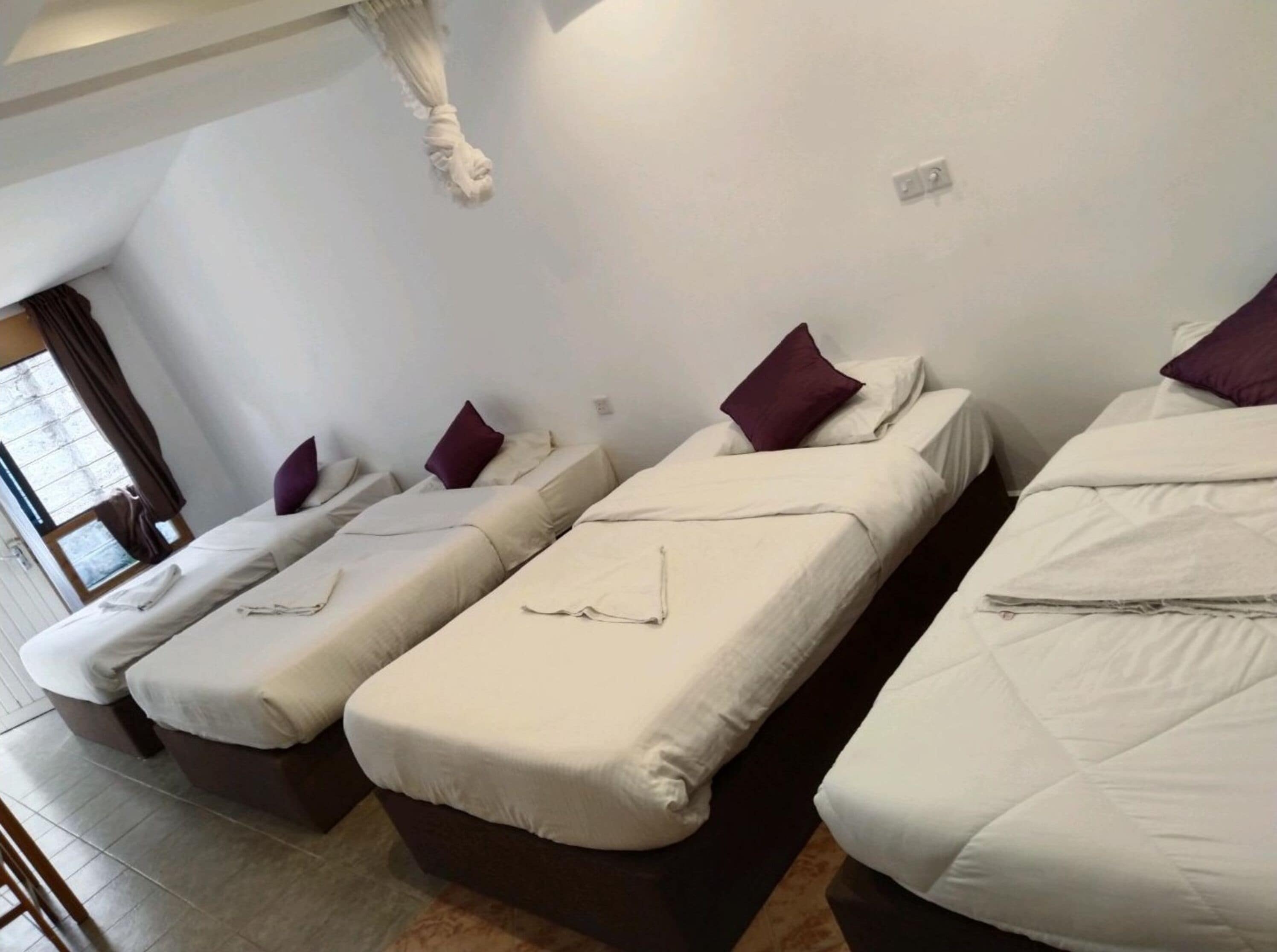 A hotel room with three single beds, each with a pillow and a blanket.