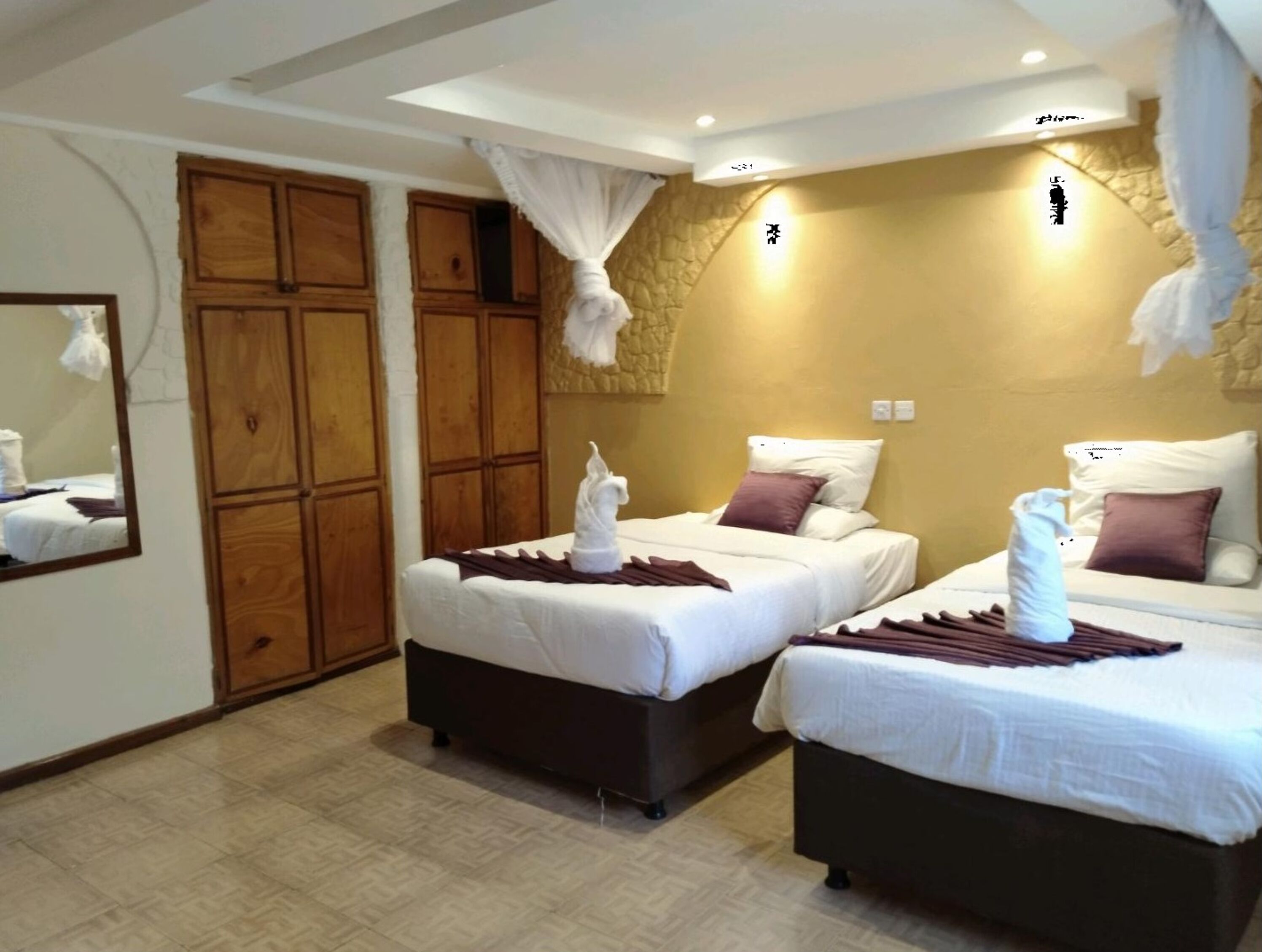 Habitación de hotel con dos camas, armario de madera, pared de piedra y un espejo.