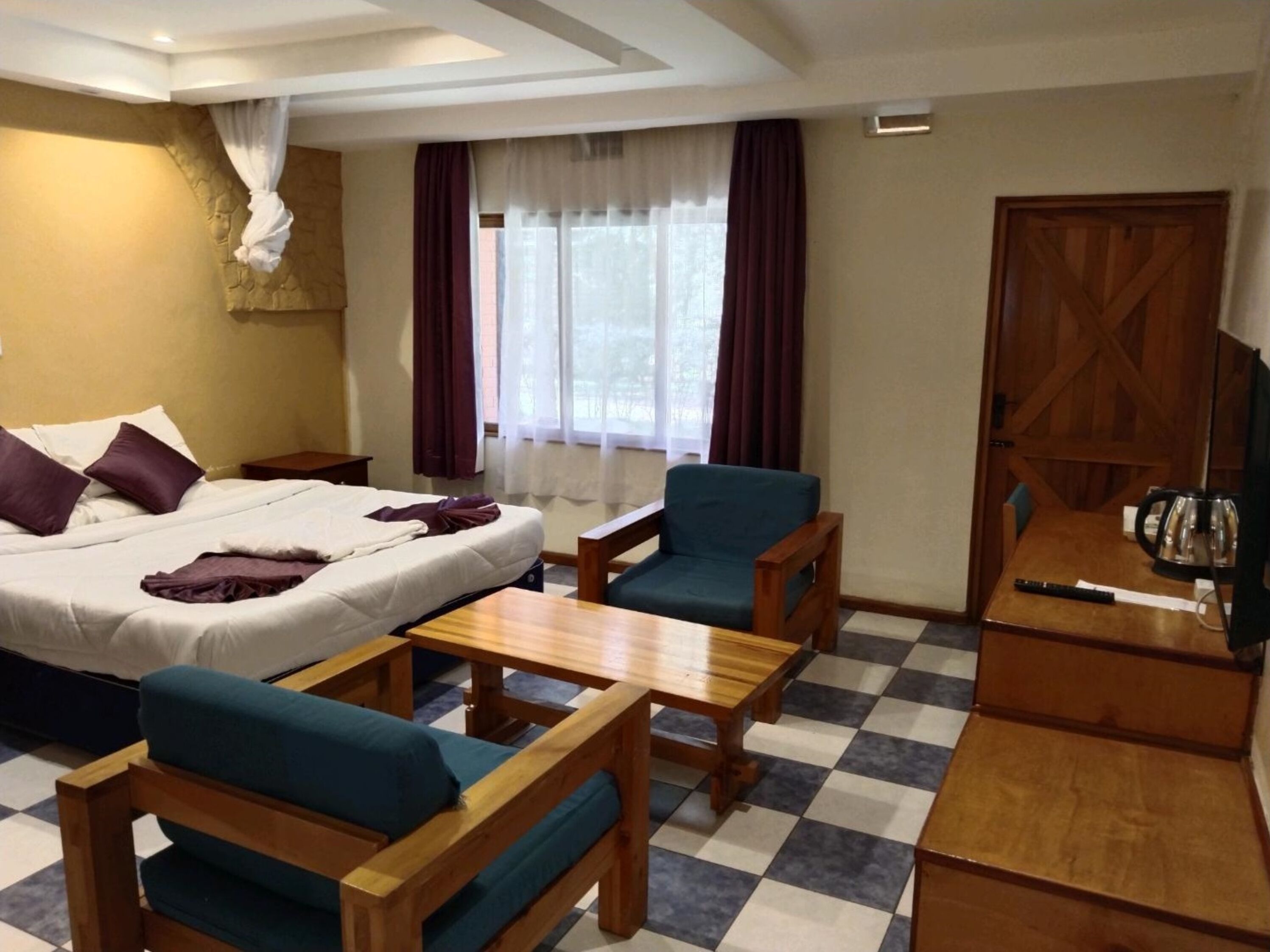 Een hotelkamer met een bed, twee stoelen, een tafel, een televisie en een raam met gordijnen.