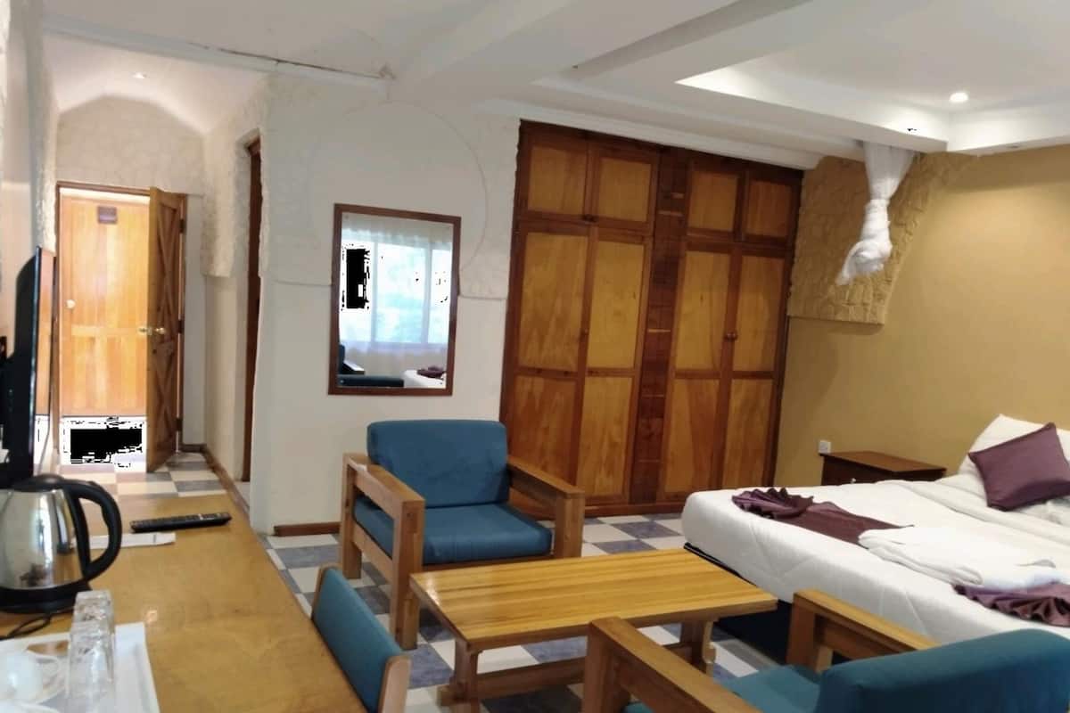 A room with a bed, a sofa, a table, and a chair. There is a window with a view of the outside.