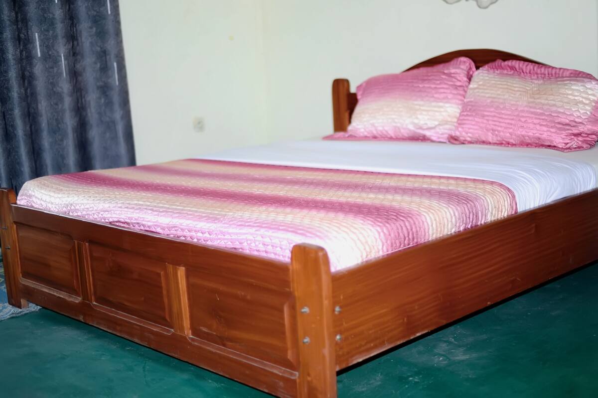 A wooden bed with a pink and white striped bedspread and pillows.