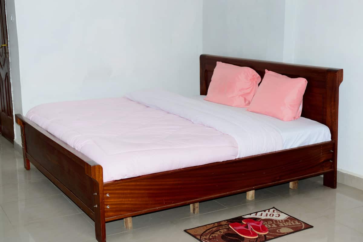 A wooden bed with a pink and white bedspread and two pink pillows.