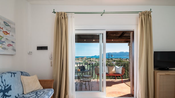 A room with a sofa, a TV, and a sliding glass door leading to an outdoor patio with a table and chairs. - Sea Shell 28 - a sea-view escape (Olbia)