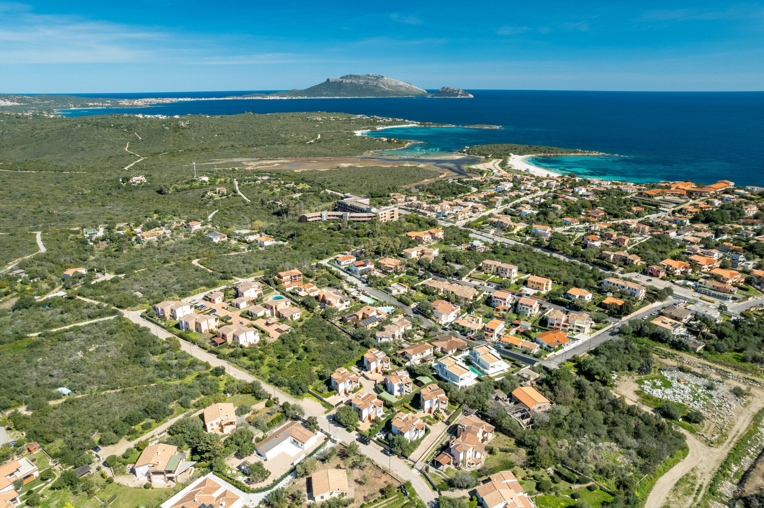 Vue aérienne d’une zone résidentielle côtière, avec des maisons, des routes et une montagne en arrière-plan.