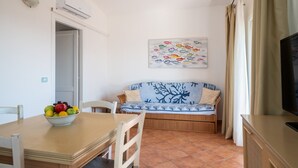 A dining area with a table, chairs, a bowl of fruit, a sofa, and a television. - Sea Shell 28 - a sea-view escape (Olbia)