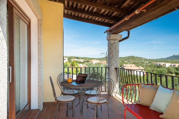 A balcony with a table and chairs, a laptop, and a red bench.