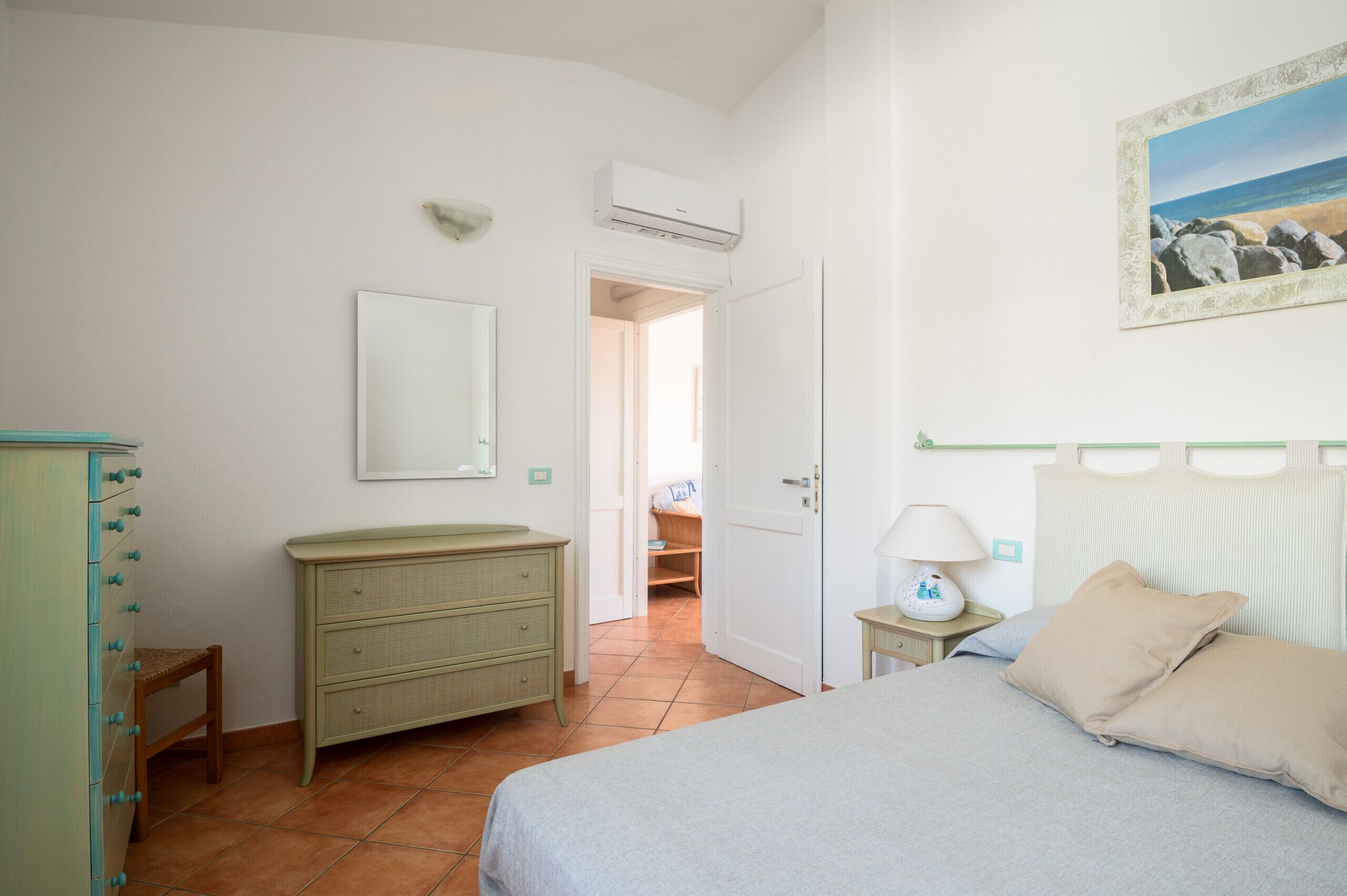 A bedroom with a bed, dresser, mirror, and a painting on the wall.