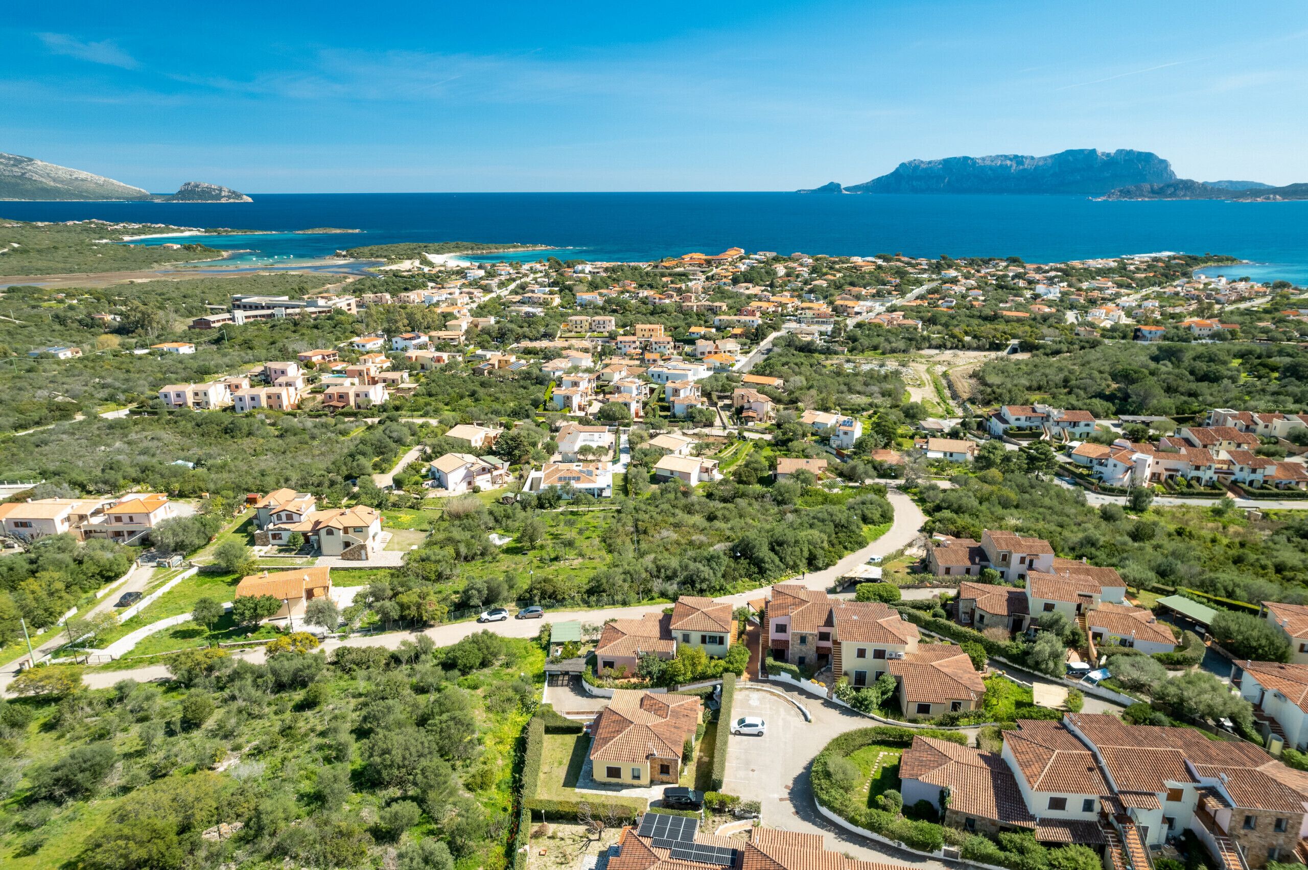 An aerial view of a coastal residential area with houses, roads, and a coastline.