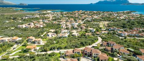 An aerial view of a coastal residential area with houses, roads, and a coastline.