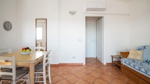 A room with a dining table, chairs, a fruit bowl, a sofa, a mirror, and an air conditioning unit. - Sea Shell 28 - a sea-view escape (Olbia)