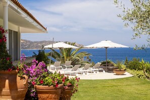 A patio with white umbrellas, lounge chairs, and a view of the sea.