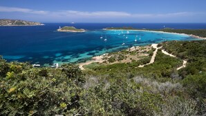 Paisagem costeira com águas azul-claras, barcos e um caminho serpenteando pela vegetação.
